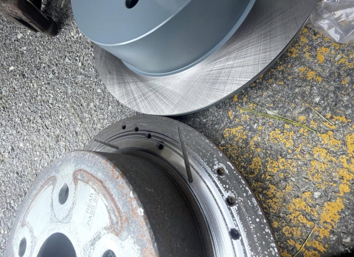 Worn drilled brake rotor next to its brand-new replacement on a driveway brake job